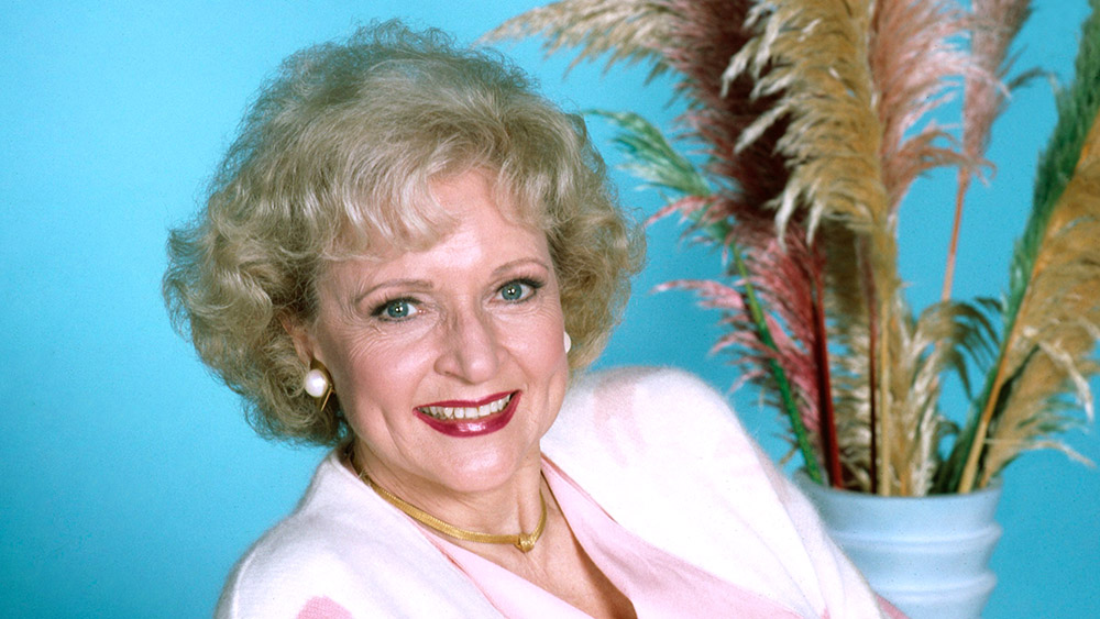 Closeup of Betty White, smiling with a vase of feathers in background.